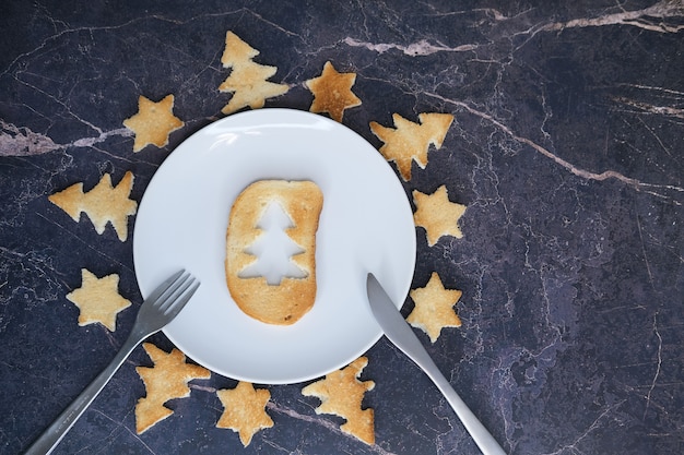 Torrada de pão em forma de árvore de Natal e estrelas deita-se em um prato branco, close-up. Foco seletivo.