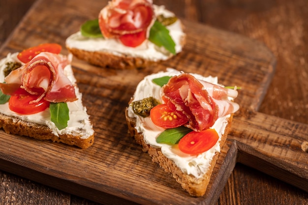 Torrada de sanduíche aberto com creme de queijo, presunto e verduras na placa de madeira e fundo de madeira. Foto de alta qualidade