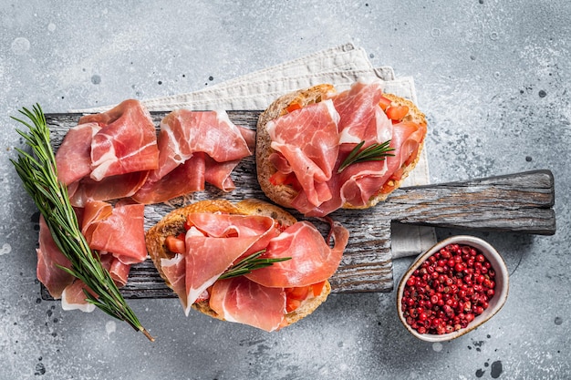 Torrada de tapas espanholas com tomate e fatias curadas de presunto ibérico de jamon na placa de madeira fundo cinza vista superior