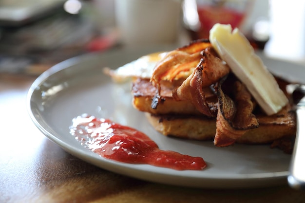 Torrada francesa de café da manhã com ovo de bacon e queijo com geléia no fundo da mesa de madeira