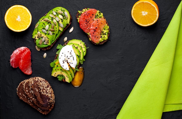 Foto torradas com abacate, sementes de gergelim, toranja, laranja, ovo e café em um fundo preto concreto. delicioso café da manhã com café e torradas