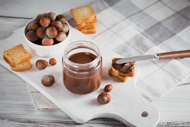 Torradas com pasta de chocolate de avelã doce no café da manhã na parede de madeira branca