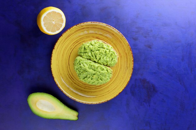 Torradas e abacate verde e limão amarelo sobre um fundo azul Torradas de café da manhã saudável com quebra de abacate em um prato amarelo Conceito de comida vegetariana Closeup