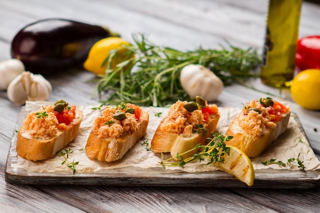 Torradas pequenas com carne de peixe. Alcaparras e rodelas de limão. Bruschetta com salmão e tomate. Refeição extremamente deliciosa.