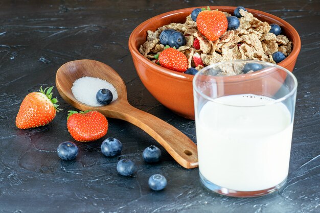 Torrado, flocos de frutas de arroz com frutas e um copo de leite sobre o fundo preto.