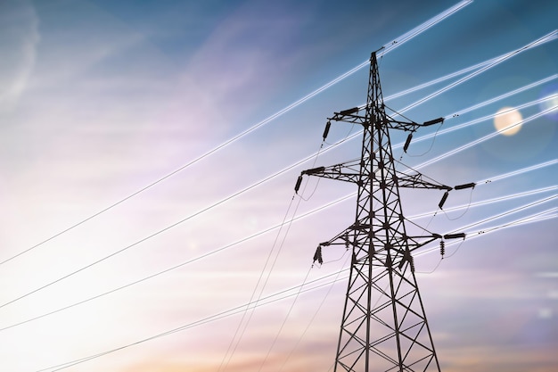 Torre de alta tensión con cables luminosos al atardecer infraestructura energética de fondo
