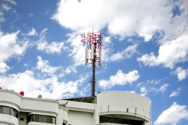 Torre de comunicación con antenas en la parte superior del edificio y cielo azul brillante con fondo de nubes