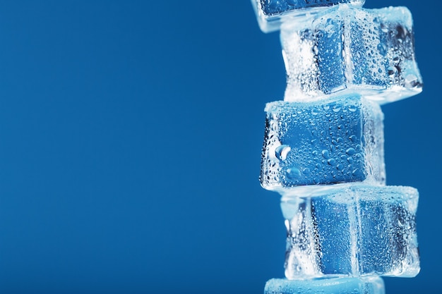 Torre de cubitos de hielo con gotas de agua en una fila sobre un fondo azul.