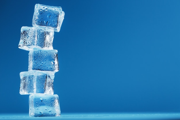 Torre de cubitos de hielo con gotas de agua en una fila sobre un fondo azul.