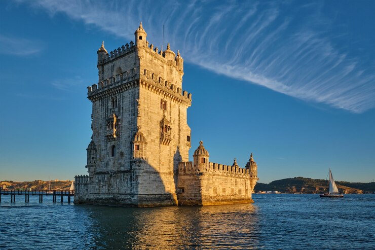 Foto torre de belem ao pôr-do-sol em lisboa, portugal, com um iate turístico
