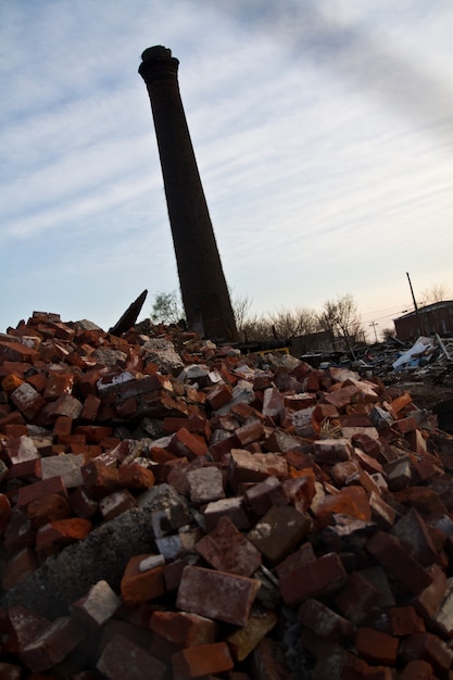 Torre de fumaça da fábrica recortada contra o céu com grandes pilhas de tijolos em primeiro plano