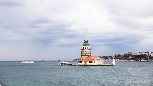 Torre de Leander localizada no meio do estreito de Bósforo, tempo nublado, navio em movimento e cidade ao longe Istambul, Turquia