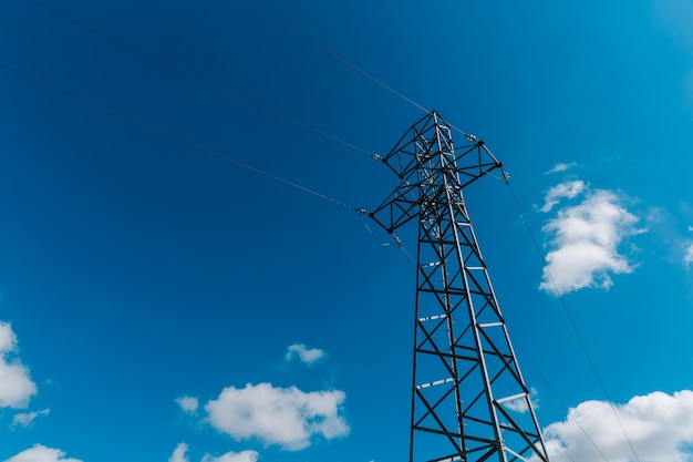 Torre de metal de alta tensão contra o céu azul com nuvens brancas