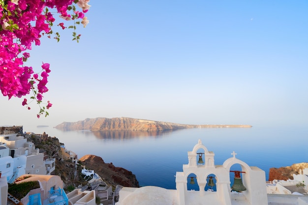 Torre de sino de igreja branca sobre o mar e a caldeira, ilha de Santorini com flores