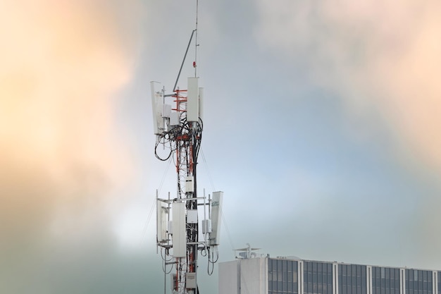 Torre de telecomunicações perto do edifício Antenna Radio e polo satélite no céu cinza Comunicação