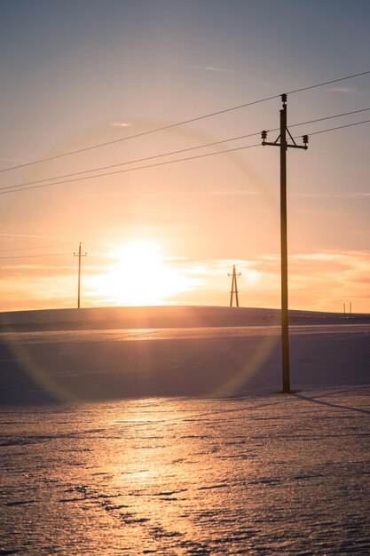 Torre eléctrica en un campo nevado El sol se pone colores naranjas paisaje nocturno