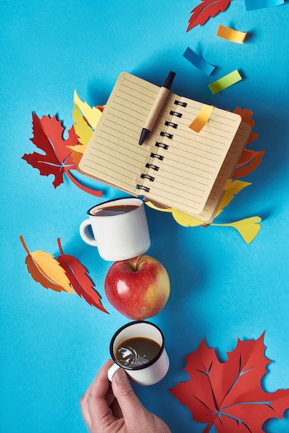 Torre de equilibrio de tazas de café, hojas de otoño y cuaderno en blanco