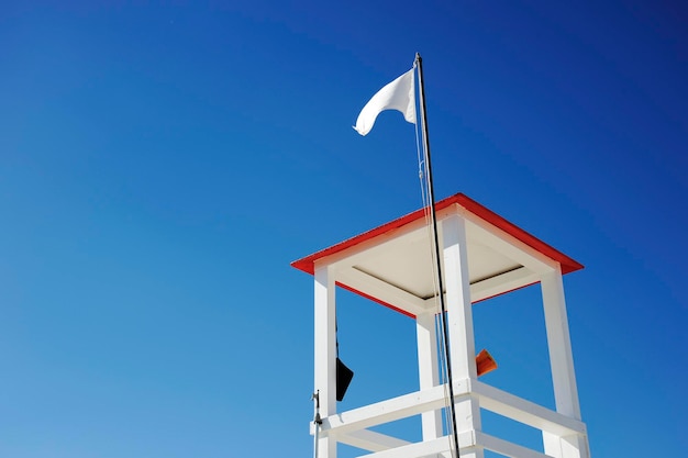 Torre de madera de salvavidas en la playa contra el cielo azul Megáfono y otras herramientas cuelgan de la torre La bandera blanca ondeando en el techoCopiar espacio para texto Concepto de riesgo y rescate