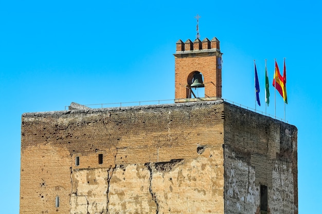 Torre medieval de la Alhambra de Granada con bandera y campanas.