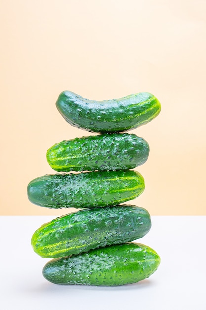 Una torre de pepinos enteros frescos en un espacio ligero y neutro. Concepto de cosecha de vegetales, alimentos orgánicos saludables. Minimalismo, espacio de copia.