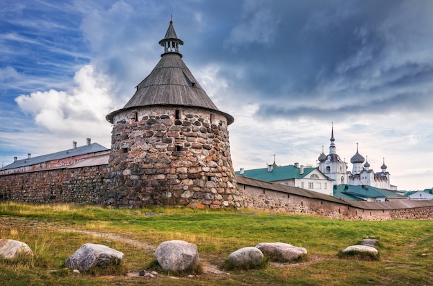 Torre de piedra Korozhnaya del monasterio Solovetsky bajo una nube oscura y piedras sobre el césped