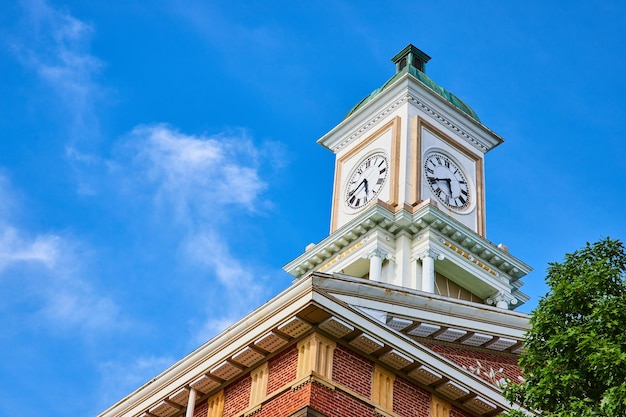 Torre del reloj en el techo de un edificio de ladrillo con cielos azules y copa de árbol verde