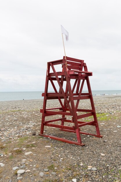 La torre roja de salvavidas en la playa de guijarros de la ciudad turística está fuera de temporada. No hay gente, playa vacía. Invierno, nubes. Montañas al fondo. Foto de alta calidad