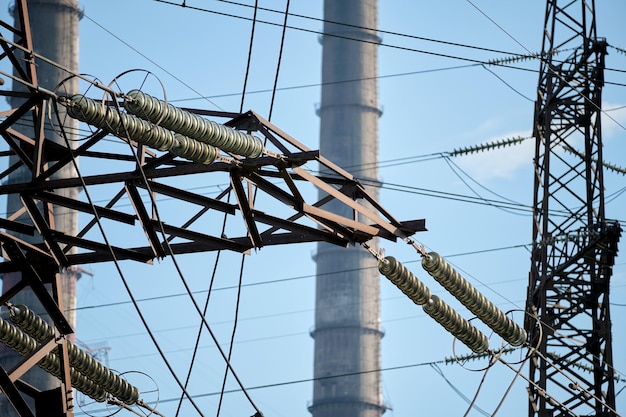 Torres eléctricas de alta tensión contra tuberías altas de plantas de energía de carbón con humo negro moviéndose hacia arriba contaminando la atmósfera. Producción de energía eléctrica con concepto de combustibles fósiles.