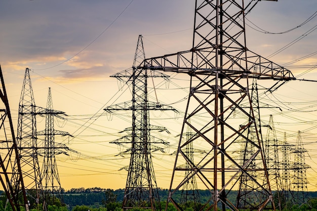 Torres eléctricas que llevan el suministro de energía a través de un paisaje rural durante la puesta de sol Enfoque selectivo