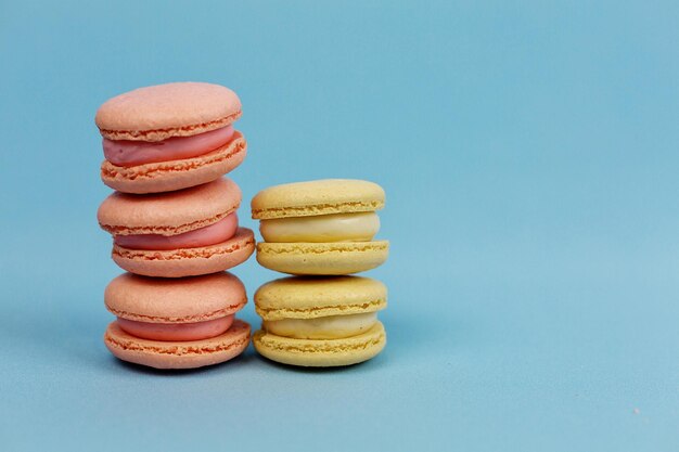 Torres de pasteles de macarrones en tonos pastel amarillos y rosas sobre un fondo azul