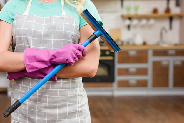 Foto torso de una mujer con delantal con limpiaparabrisas de plástico de pie en la cocina