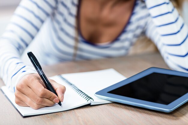 Foto torso de mujer escribiendo en cuaderno por tableta digital