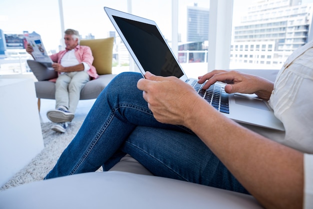 Torso de mujer usando laptop mientras hombre leyendo periódico