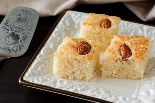 Torta árabe tradicional de la sémola de Basbousa del primer tres pedazos con agua anaranjada Nuts del almendra de la almendra. Copia espacio Fondo oscuro