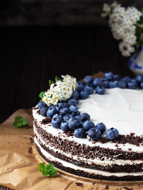 Torta casera de cerezas de ave con crema agria, decorada con arándanos y hojas de menta sobre papel de hornear