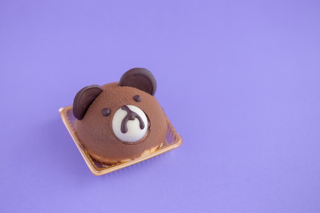 Torta de chifón de chocolate con cabeza de oso de peluche marrón sobre fondo violeta