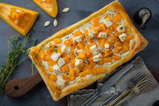 Torta com abóbora, queijo feta, ricota e tomilho sobre um fundo escuro de concreto.