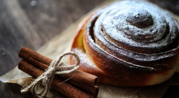 Torta com canela e maçãs em uma mesa de madeira. Pastelaria fresca com paus de canela com nozes e açúcar em pó. Pão com nozes e canela na mesa.