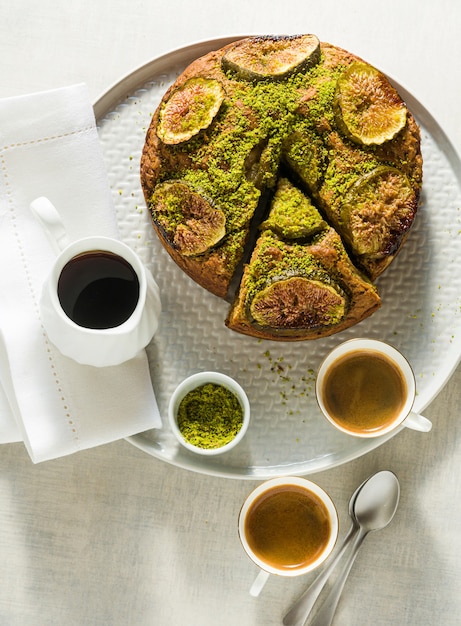 Torta com figos e pistache em uma mesa com xícaras de café expresso e xarope de bordo. café da manhã ou brunch de verão