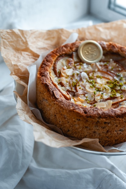 Foto torta com queijo dor blue, peras e amêndoas, inteira em um prato sobre uma mesa branca