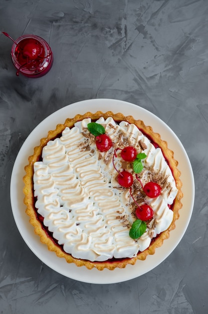 Torta com recheio de cereja e merengue italiano com um cocktail de cereja, chocolate e hortelã por cima em um prato branco sobre um fundo escuro e concreto.