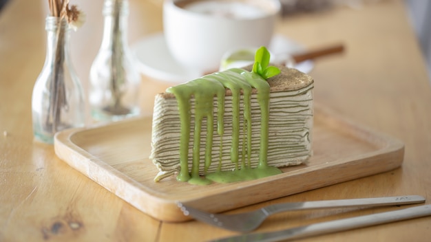 Torta de crepe del té verde con la hoja de té verde en la placa de madera.