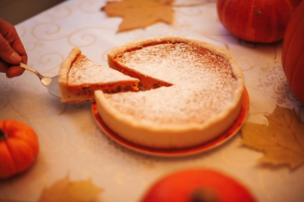 Torta de abóbora caseira com açúcar de confeiteiro nas folhas de outono e abóboras laranja na mesa da cozinha Pedaço de torta de outono na espátula de metal closeup comida tradicional para o Dia de Ação de Graças e feriados de Halloween