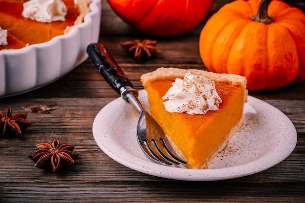 Torta de abóbora caseira para ação de Graças com chantilly e canela em fundo de madeira