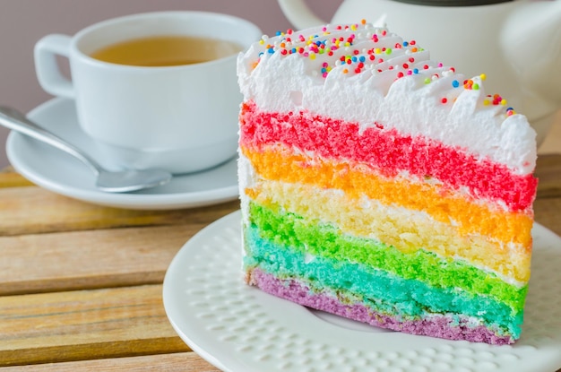 Torta de arco-íris com xícara de chá branca na mesa de madeira