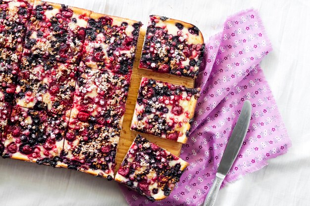 Torta de baga e requeijão cortada em fatias quadradas em uma placa de madeira vista superior plana