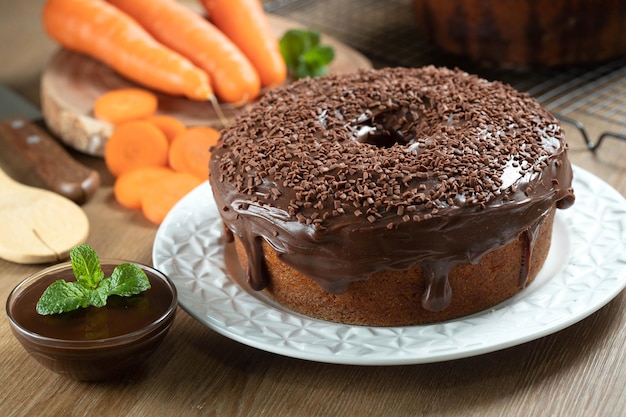 Torta de cenoura brasileira com cobertura de chocolate em mesa de madeira com cenouras ao fundo