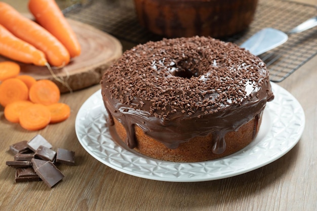 Torta de cenoura brasileira com cobertura de chocolate em mesa de madeira com cenouras ao fundo