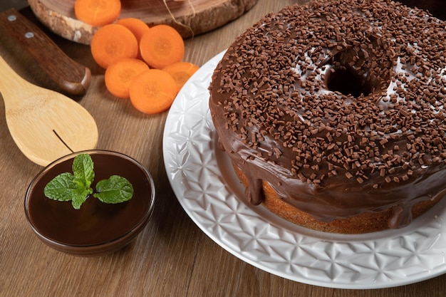 Torta de cenoura brasileira com cobertura de chocolate em mesa de madeira com cenouras ao fundo