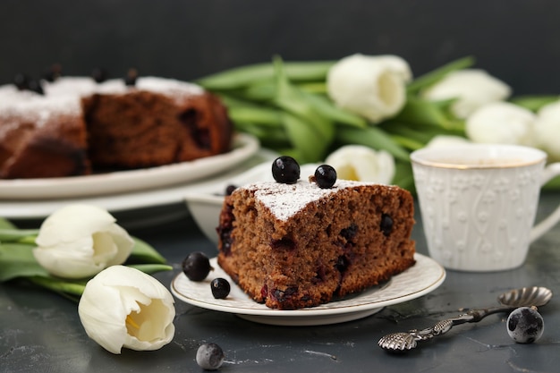 Torta de chocolate com groselha preta, na mesa há uma xícara de café e tulipas brancas